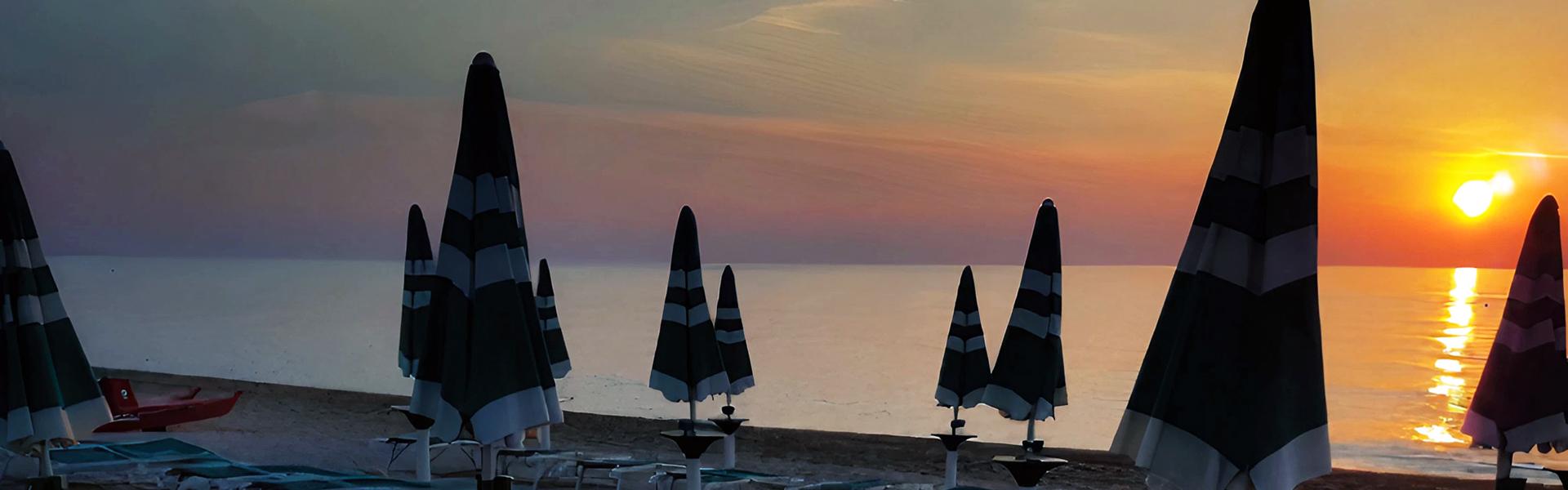Spiaggia al tramonto con lettini e ombrelloni chiusi, atmosfera serena.