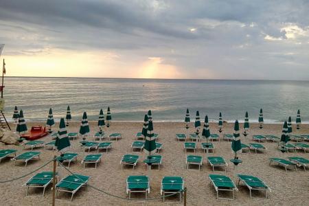Spiaggia al tramonto con ombrelloni chiusi e lettini vuoti.