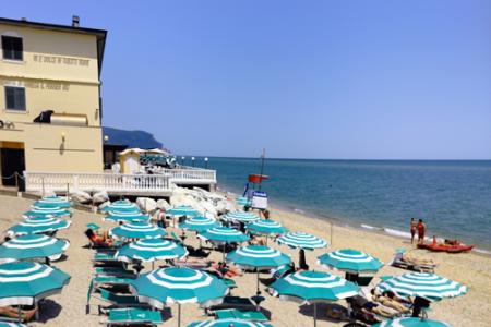 Spiaggia affollata con ombrelloni verdi e bianchi, vista mare e bagnini.