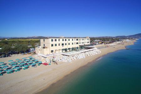 Spiaggia con ombrelloni verdi e edificio fronte mare, giornata limpida e soleggiata.