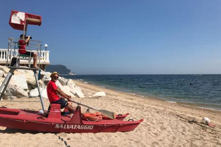 Bagnino in spiaggia con pattino di salvataggio e torretta di avvistamento.