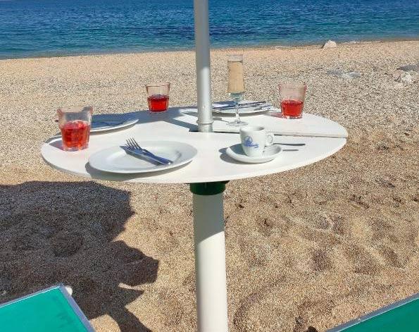 Tavolo sulla spiaggia con bicchieri di bevande rosse e tazzina di caffè.