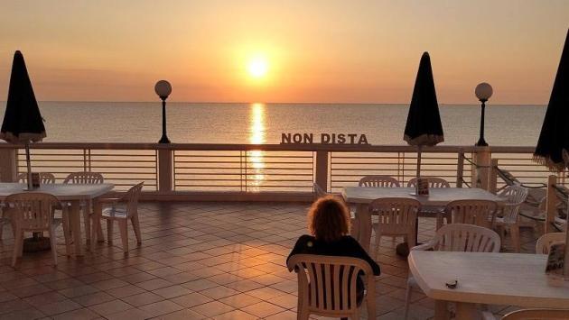 Tramonto sul mare visto da una terrazza con sedie bianche e ombrelloni chiusi.