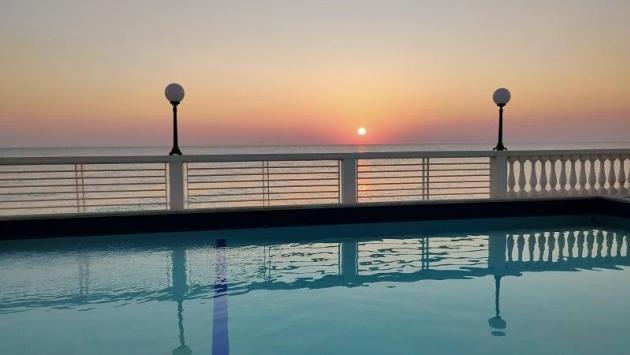 Piscina al tramonto con vista mare e cielo arancione.