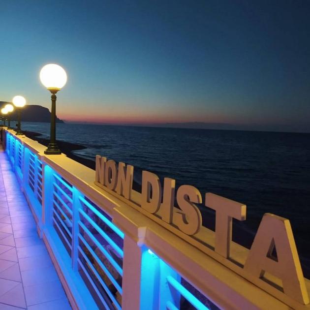 Passeggiata serale sul mare con luci blu e vista sul tramonto.