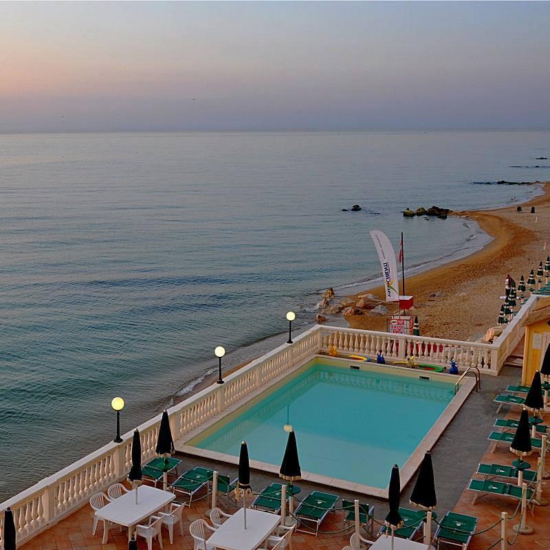 Piscina sul mare con vista panoramica e spiaggia sabbiosa al tramonto.