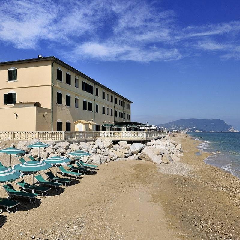 Spiaggia sabbiosa con ombrelloni e edificio lungo la costa.
