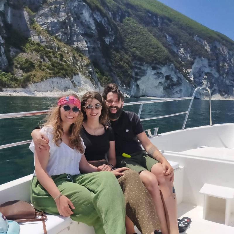 Tre amici sorridenti su una barca, con scogliere verdi e bianche sullo sfondo.